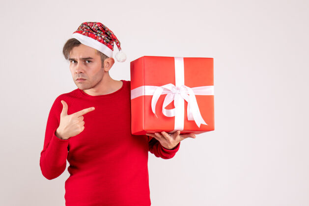 可爱前视图：戴圣诞帽的年轻人指着白色背景上的礼物礼物礼物微笑