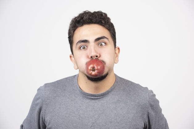 肖像穿着灰色运动衫的年轻人在灰色衣服上摆着红苹果的姿势食物新鲜男孩