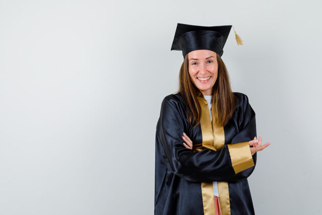 笑女毕业生的画像 展示了一些东西 而笑着在学术服装和看起来有趣的前视图毕业典礼妇女成就