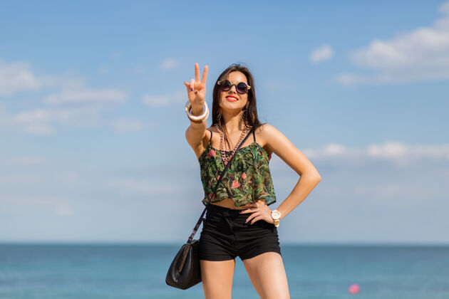 身体穿着时髦的热带服装的女人在海滩上摆姿势自然心情太阳镜