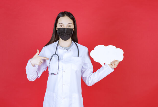 空白女医生带着听诊器 戴着黑色面罩 手里拿着一张云状的空白问讯台居家制服外科