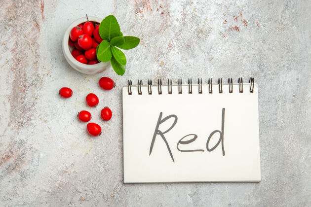 新鲜顶视红色水果与红色书写记事本上的白色表浆果红色水果树枝叶子书写