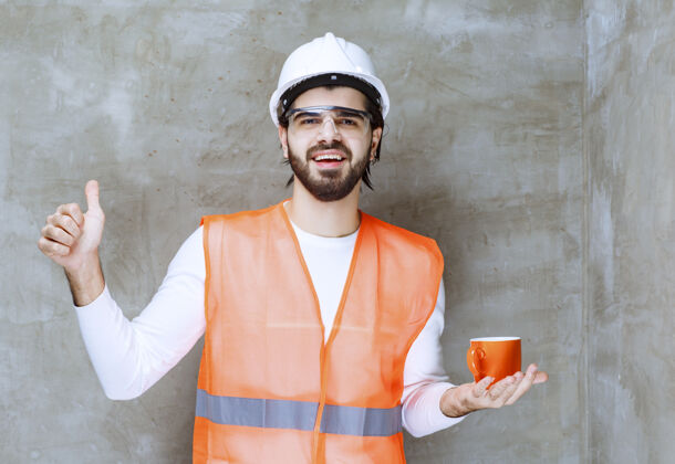 员工戴着白色头盔的工程师拿着一个橙色的杯子 享受着饮料的味道刷新茶年轻人