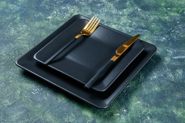晚餐前视图黑色盘子 黑色背景上有金色的刀叉金色钢笔深色
