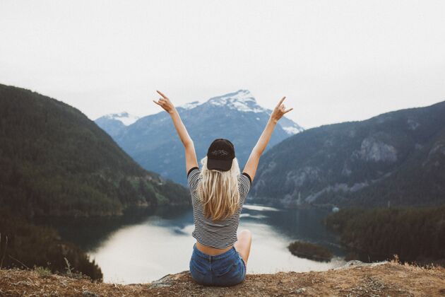 肖像年轻的金发女孩坐在悬崖上欣赏着山和湖的景色年轻短裤金发