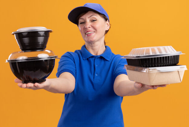 站着身穿蓝色制服 头戴鸭舌帽的中年女送货员站在橘色的墙上 手里拿着食品包 开心而积极地看着前面抱着快乐正面