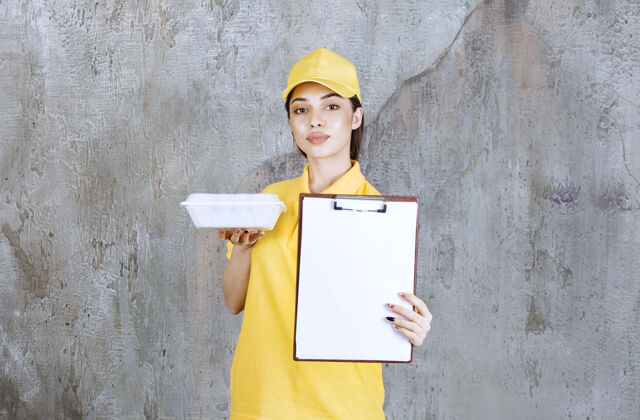 成人穿着黄色制服的女服务人员拿着一个塑料外卖盒 要求签名邮件清单年轻人
