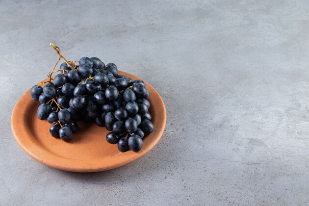 石头一束新鲜的黑葡萄放在石头桌上的泥盘里新鲜食物盘子
