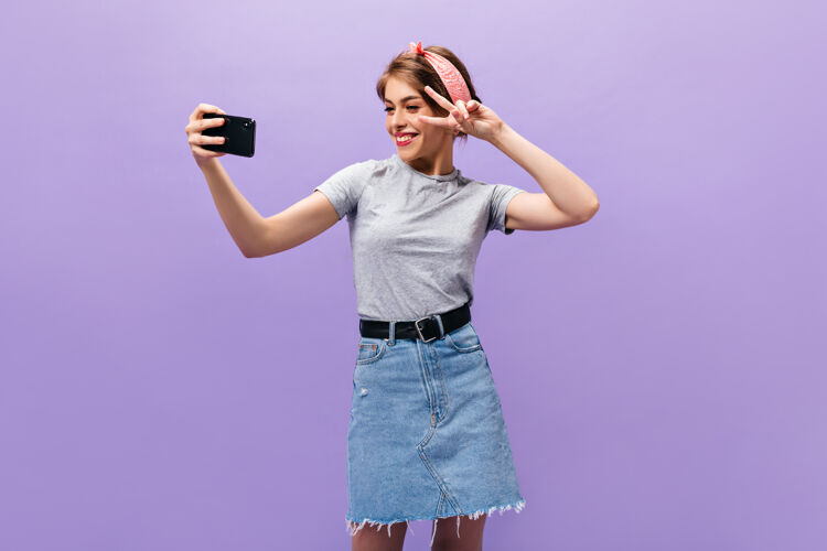 复制展示和平标志的女孩 在紫色背景上眨眼和自拍穿着时髦服装摆姿势的漂亮年轻女子头发姿势紫色