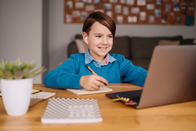 互联网一个未成年男孩用笔记本电脑和他的老师打视频电话 在线上课 做笔记显微镜耳机学习
