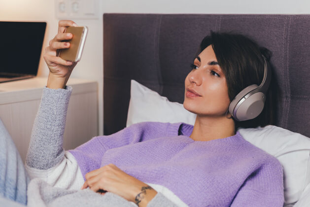 枕头快乐的女人在家舒适的床上穿着暖和的衣服套头衫 听音乐舒适瞌睡年轻
