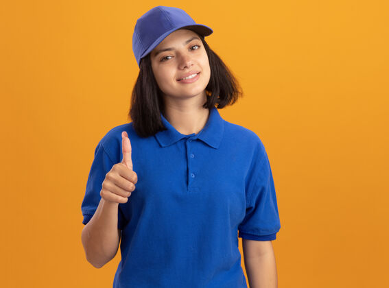 拇指身穿蓝色制服 头戴帽子的年轻送货员友好地站在橙色的墙上 竖起大拇指朋友制服递送