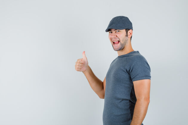 小年轻的男人戴着灰色的t恤帽子 露出拇指 看起来很高兴商务网络摄像头接听电话电子连接