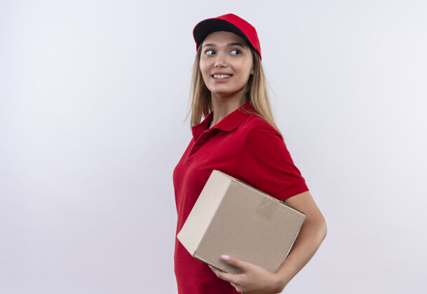 制服看着面带微笑的年轻送货女孩 穿着红色制服 戴着帽子 盒子被隔离在白色背景上 留着复印空间递送拿着微笑