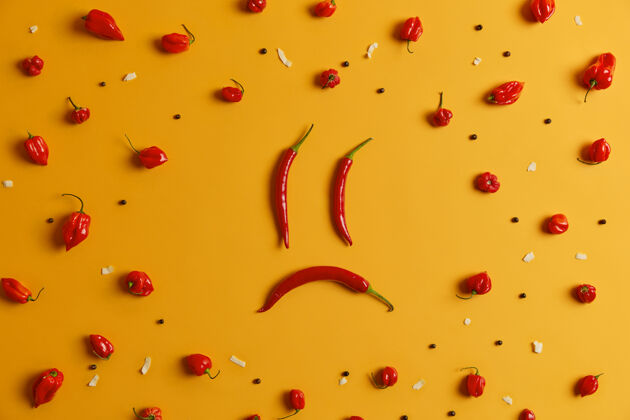 不高兴用长红辣椒做成的悲伤的人的脸 周围有胡椒的哈巴内罗辣椒 黄色的背景创意拍摄 食物艺术概念含有有益营养的辛辣成分辣味蔬菜生的空品种