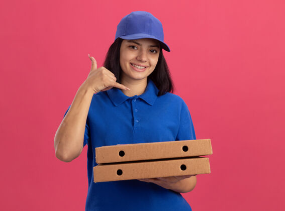 制服身穿蓝色制服 头戴鸭舌帽 拿着比萨饼盒 微笑着站在粉色墙壁上的年轻送货员披萨送货站着