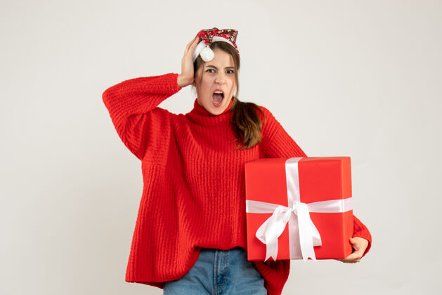 节日正面图愤怒的女孩戴着圣诞帽拿着礼物站着头漂亮抱着礼物