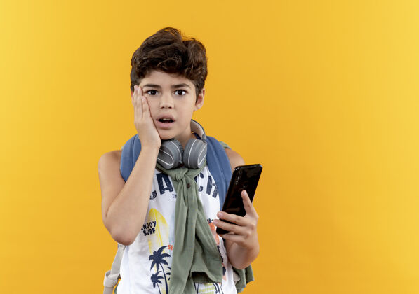 脸颊一个戴着耳机 背着书包 手放在黄色背景上的面颊上的小男孩电话关心耳机