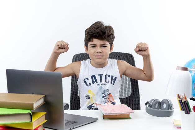 强壮自信的小男生坐在课桌旁 拿着学习工具做着强烈的手势 孤立在白色背景上工具学校手势