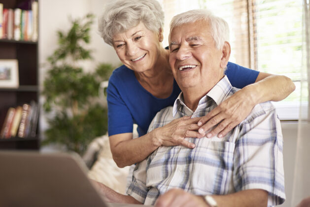 现代快乐的祖父母使用他们的数码笔记本电脑桌子老年夫妇当代