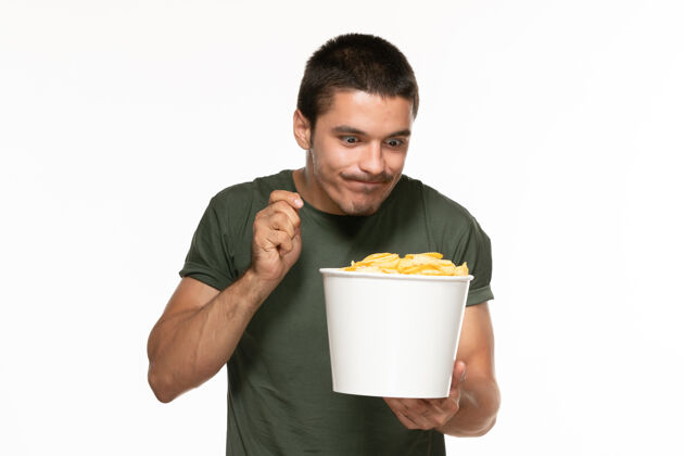 年轻男性正面图身穿绿色t恤的年轻男子拿着一个篮子 里面放着土豆 在白墙上吃着 孤独地享受着电影杯子视图电影院