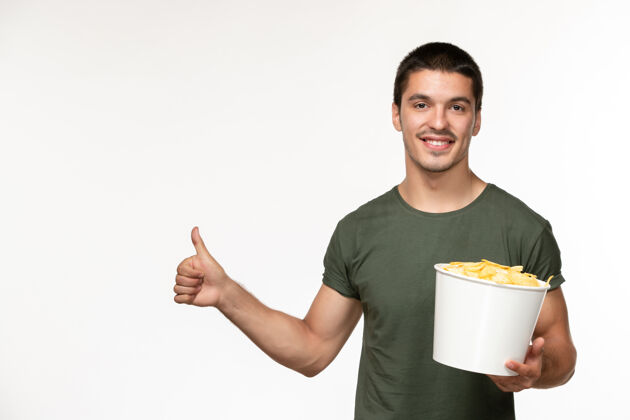 肖像正面图：身穿绿色t恤的年轻男性 带着土豆cips 微笑着站在白色的墙上看电影《孤独的人》电影院成人电影电影