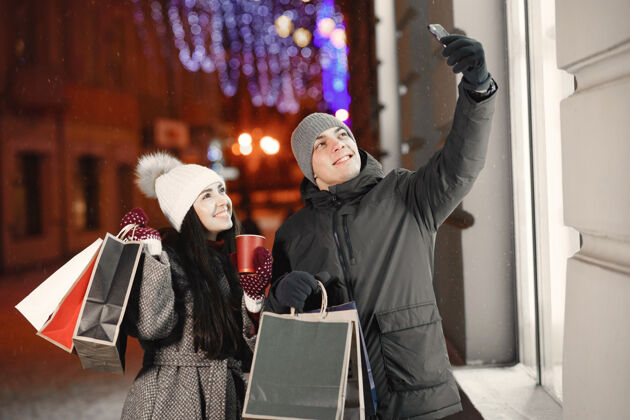 温暖带着购物袋的年轻夫妇的户外夜照购买女购物