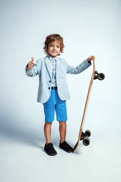 男性漂亮的小男孩在滑板上穿着休闲服在白色的工作室板滑板空气