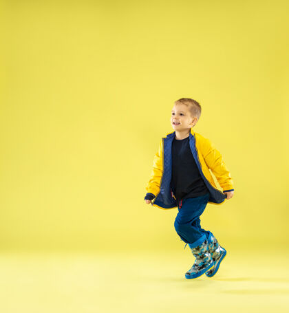 明亮一个穿着雨衣的时髦男孩在黄色的沙滩上奔跑和嬉戏的全长肖像肖像时尚学校