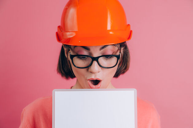 板相当惊讶的女工建设者拿着白色的空白标牌 背景是粉色的建筑头盔女士工人空间