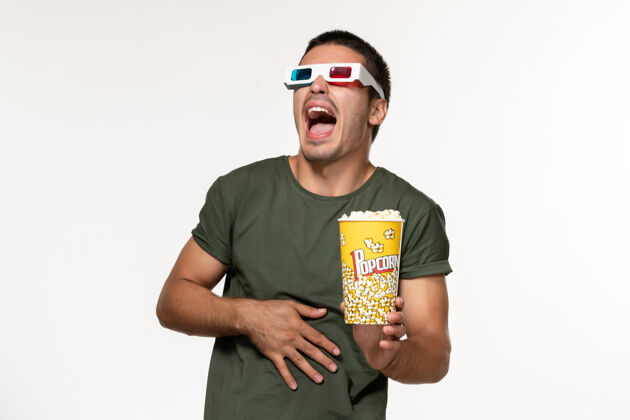 男人正面图身穿绿色t恤的年轻男性戴着d型太阳镜拿着爆米花在浅白色的表面上看电影孤独的电影男性电影电影年轻男性电影