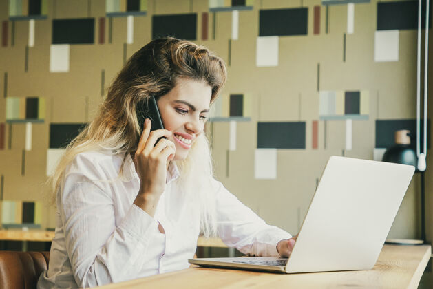 肖像积极的女企业家在工作空间里用笔记本电脑和手机交谈女性同事白种人