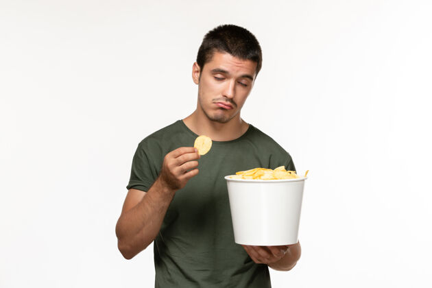 潘趣正面图：穿着绿色t恤的年轻男性 带着土豆馅饼 在白墙上吃饭 孤独的人在电影院里电影肖像杯子