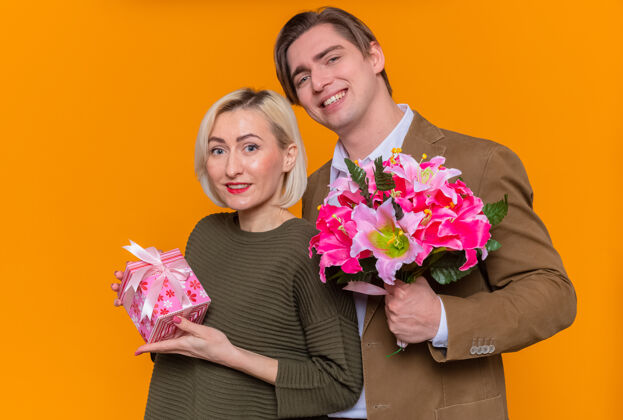 年轻年轻漂亮的情侣幸福的男人捧着花束和女人一起欢庆国际妇女节站在橙色的墙上礼物花束国际