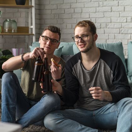 比萨饼两位男性朋友在电视上看体育节目和喝啤酒的正面图电视伙伴啤酒瓶