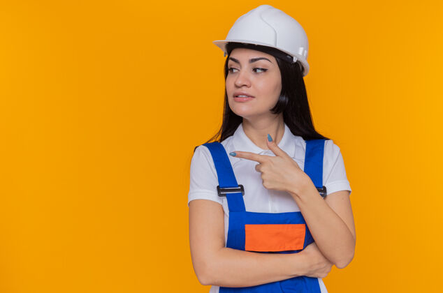 头盔身穿施工制服 头戴安全帽的年轻建筑妇女向旁边看立场建筑工人制服