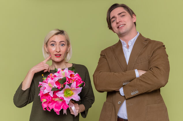 花束年轻美丽的夫妇幸福的男人和女人带着花束看着前面微笑着欢庆国际妇女节站在绿色的墙上站立年轻庆祝
