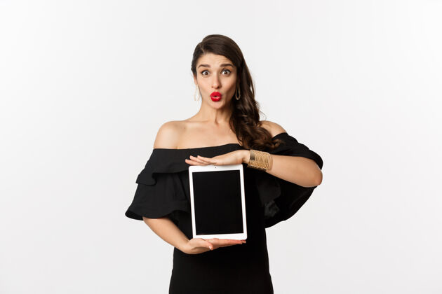 年轻时尚和购物理念红唇美女 黑色连衣裙 平板电脑屏幕上 看起来很兴奋 站在白色背景下美丽黑发表情