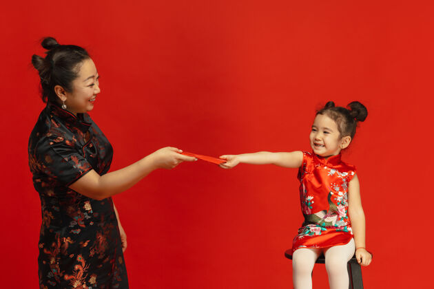 美丽送红包和微笑…亚洲母亲和女儿的肖像隔离在传统服装的红墙上庆祝 人类的情感 节日复制空间庆典祝福旗袍