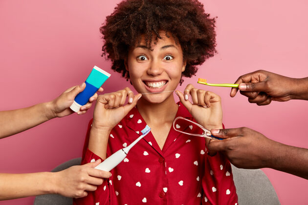 种族卷曲的女人关心牙齿 拿着牙线 周围是牙膏和刷子黑发非洲室内