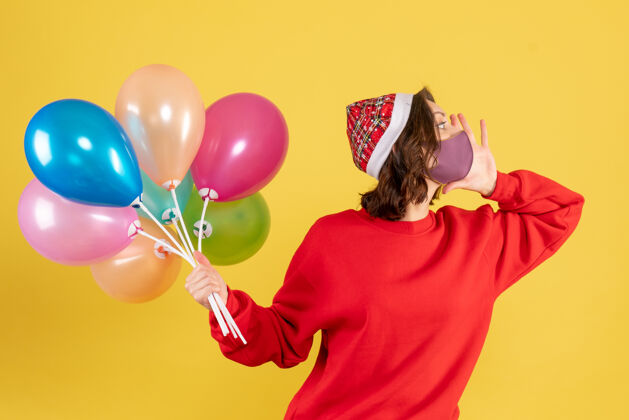 派对正面图戴着面具手持气球的年轻女子在黄色庆典派对上感慨新年彩女女人情感庆祝