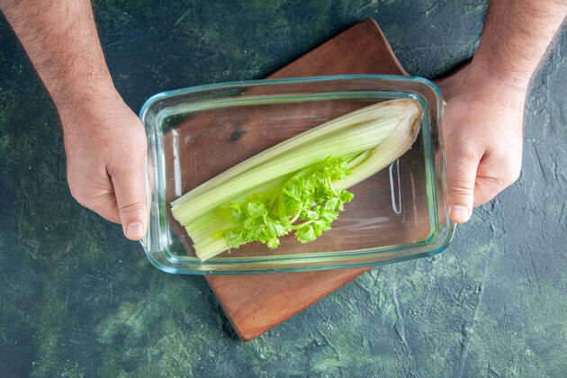 膳食顶视图男厨师拿着盘子上放着芹菜的深色餐桌沙拉减肥餐彩色照片食物健康玻璃碗蔬菜