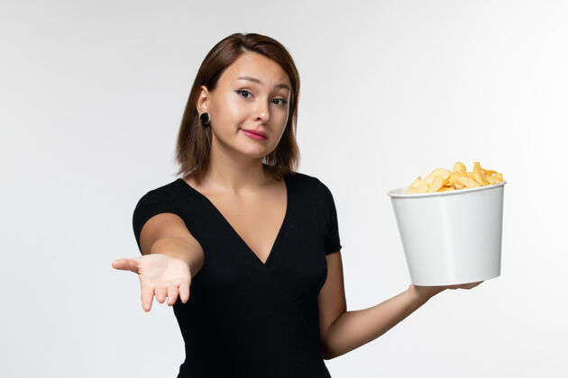 前面正面图：身穿黑色衬衫的年轻女性 手拿薯片放在浅白的表面上电影孤独举行