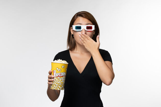爆米花正面图年轻女性戴着d型太阳镜拿着爆米花包 在白色表面看电影看抱孤独