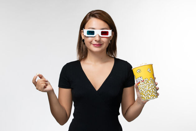 电影院正面图年轻女性拿着爆米花 戴着d型太阳镜在白色表面上看电影抱太阳镜电影