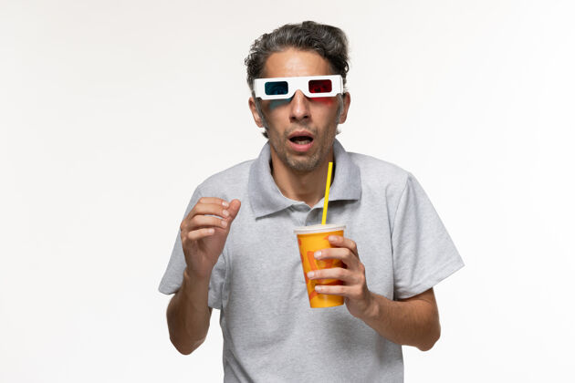 前面正面图：年轻男性戴着d型太阳镜在白色表面喝苏打水看电影男年轻的男性苏打水