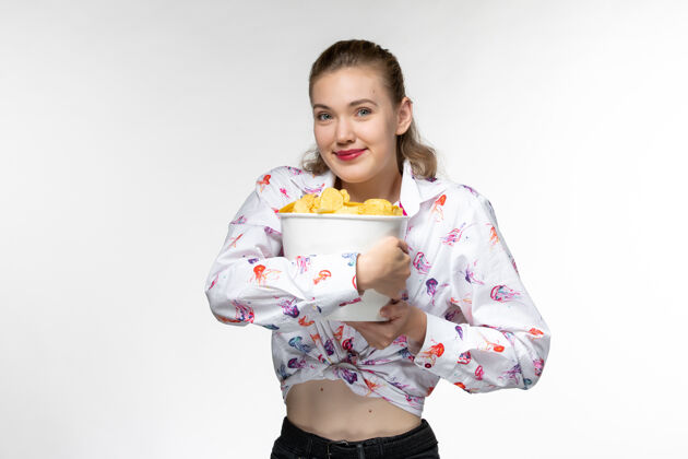 抱着正面图：年轻的女性拿着篮子 白色的表面上挂着微笑的薯片前面睡衣篮子