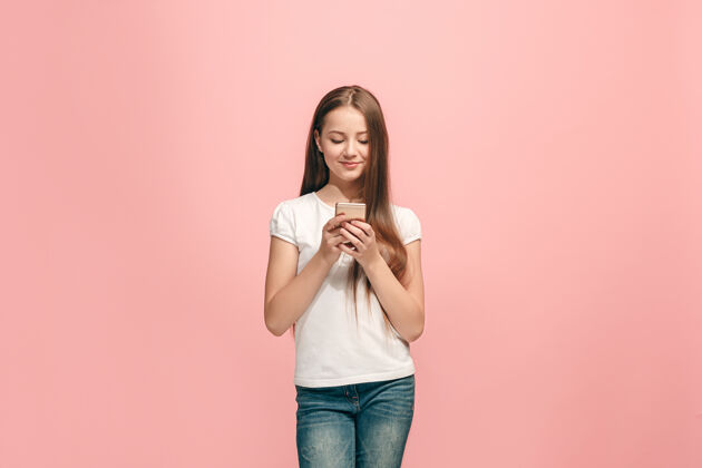 成功快乐的少女站在时尚的粉色工作室墙上 用手机微笑着快乐幸运美丽