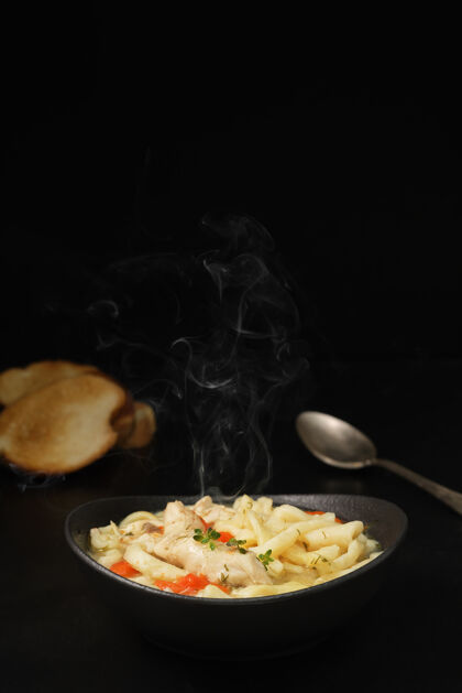 热一张深色的桌子上放着鸡汤 里面有蔬菜 香料和自制的面条复制空间汤胡萝卜