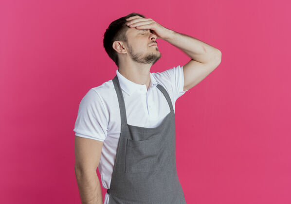 男人围着围裙的理发师站在粉红色的墙上 看上去既累又无聊理发师头站着
